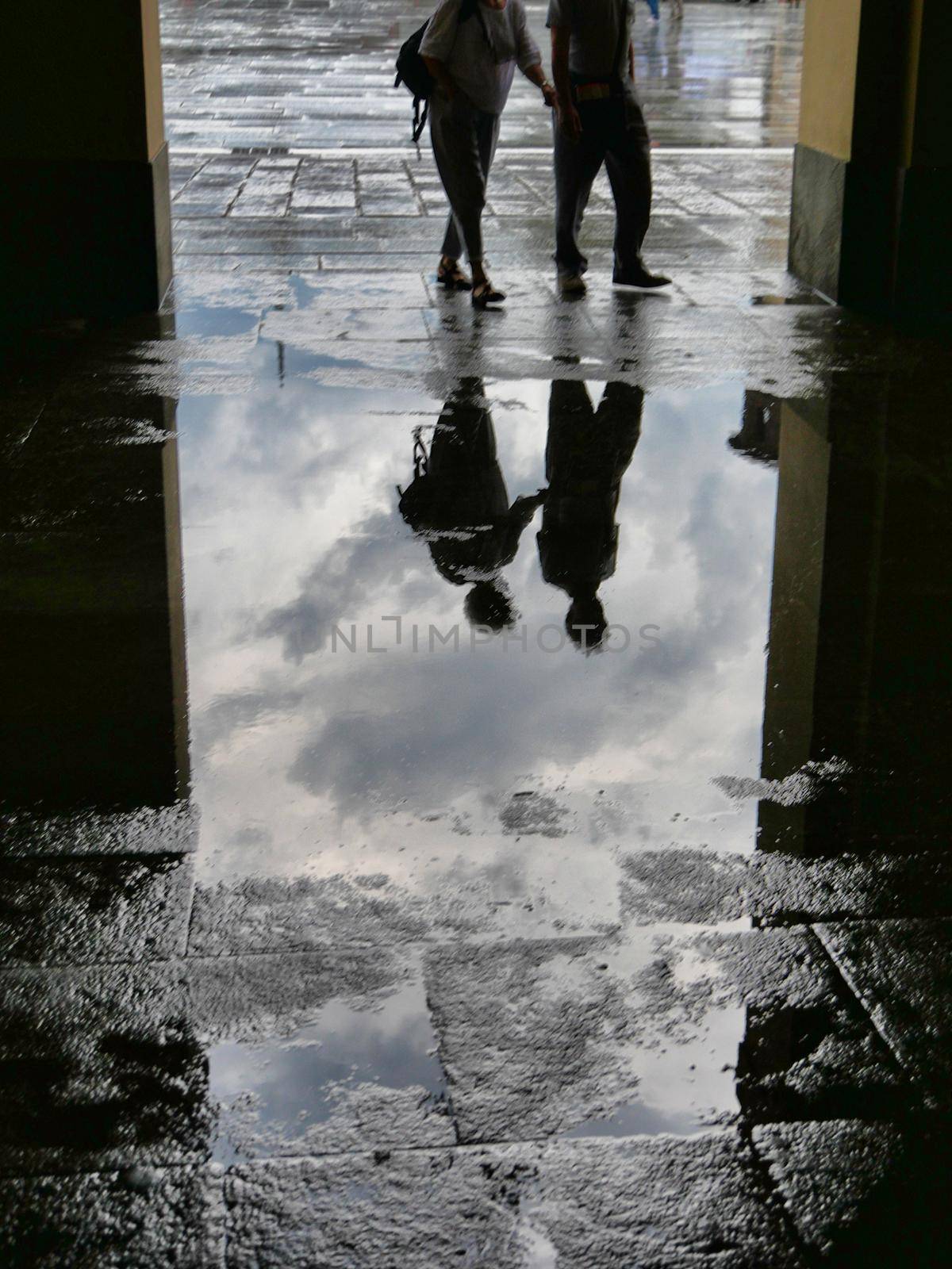 People silhouettes reflected in puddle of water after the storm by lemar