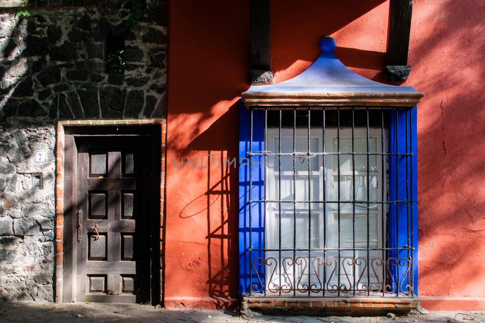Lattice window on dark orange wall next to stone wall with wooden door. Classic Hispanic houses from Mexico City. Colorful Mexican neighborhood