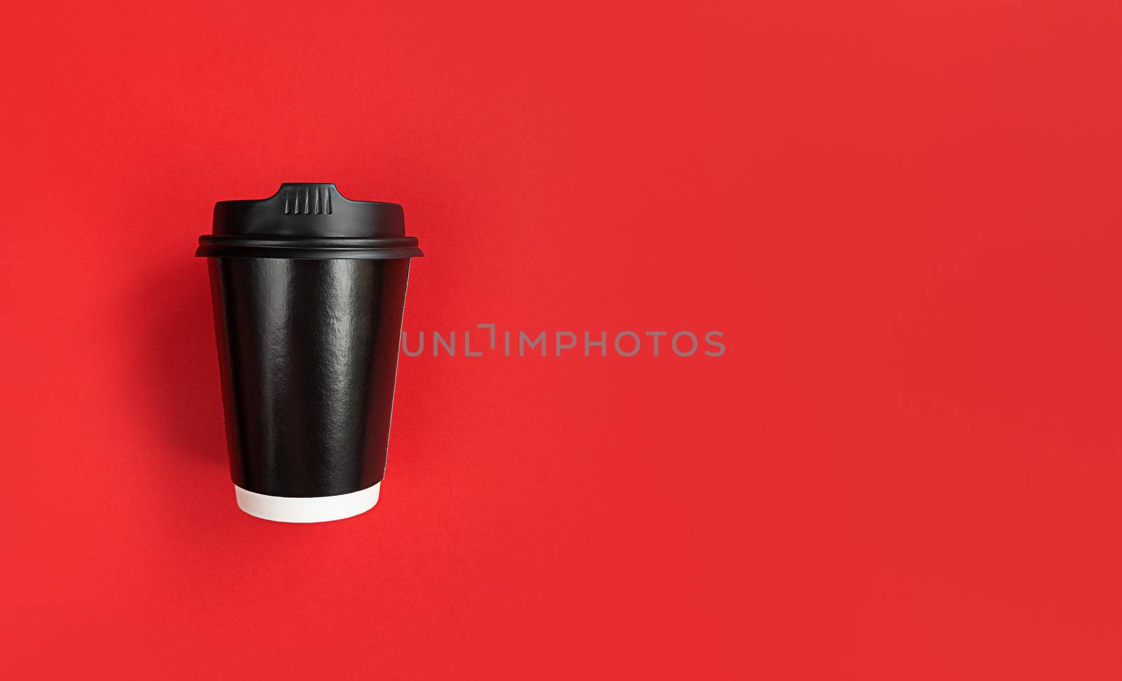 Black paper coffee cup to go on a red background with copy space.