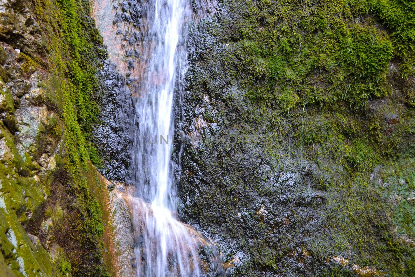 Small waterfall on a rocky stream stone background. Mountain covered with green moss.