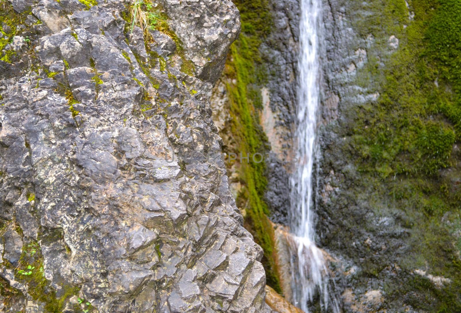 Small waterfall on a rocky stream stone background. Mountain covered with green moss.