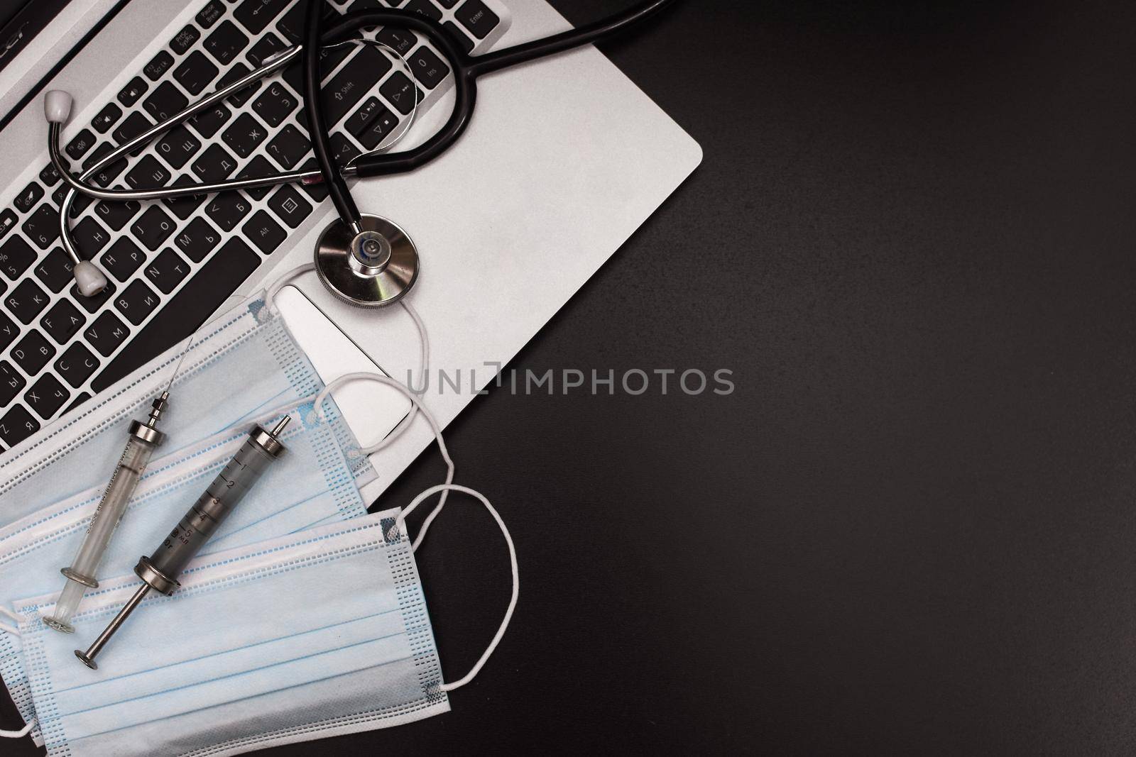 Doctor's office with modern workplace in medical clinic. Laptop, medical mask and syringes on the table top view. High quality photo