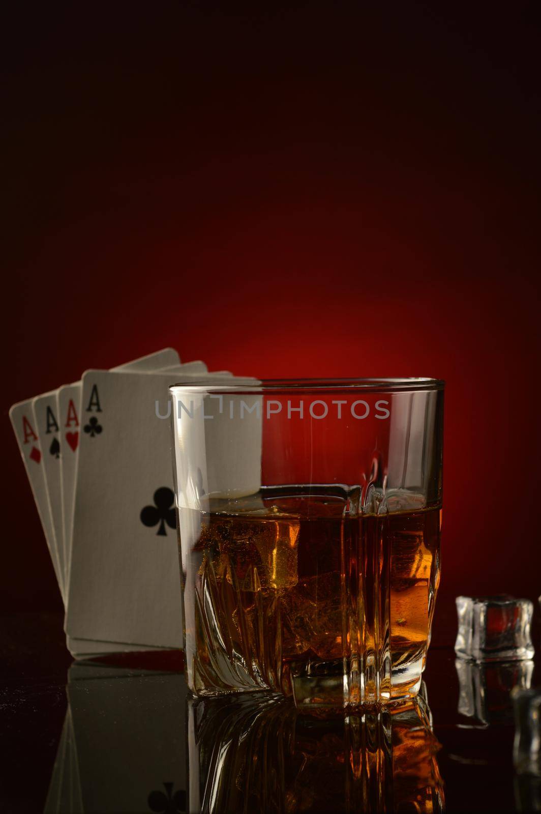 A shallow depth of field on the whiskey glass with four aces to represent a gambling mans drink.