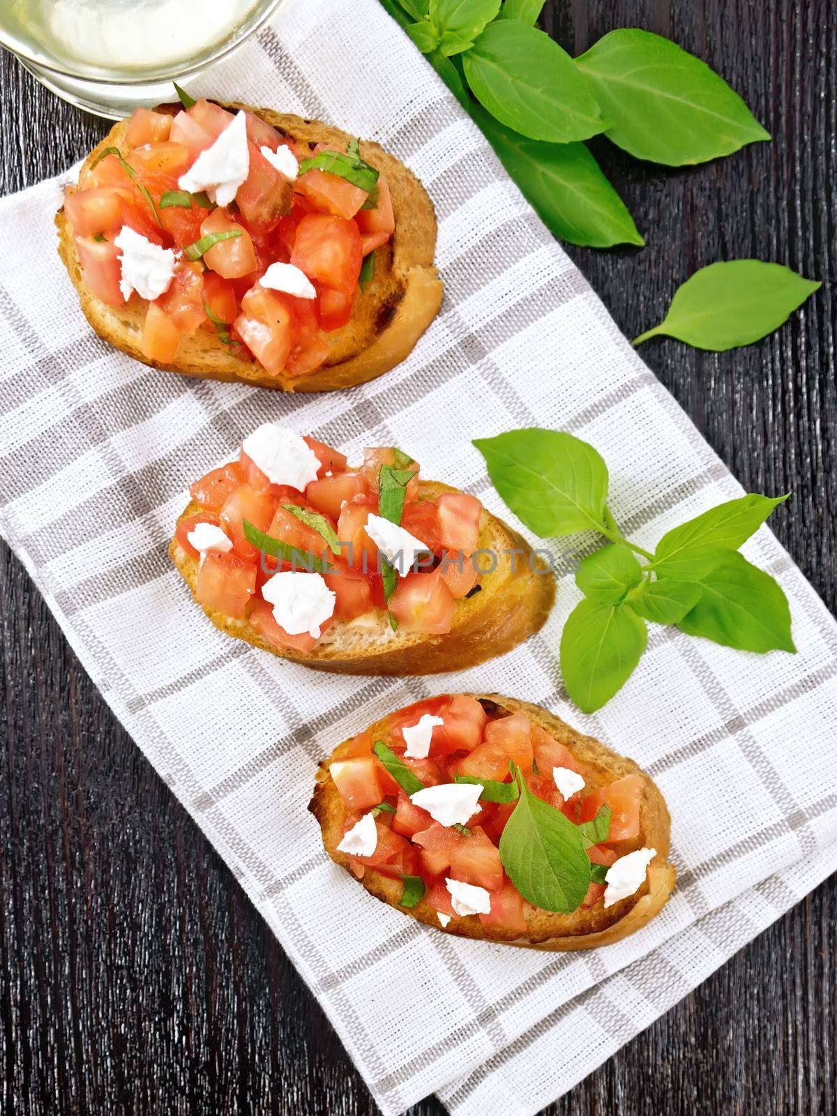 Bruschetta with tomato, basil and soft cheese on a napkin on wooden board from above