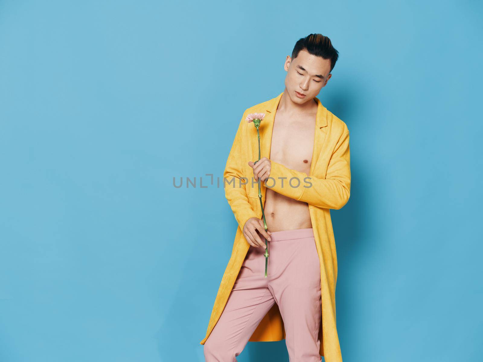 Fashionable man in a yellow coat with a flower in his hand on a blue background, Asian appearance by SHOTPRIME