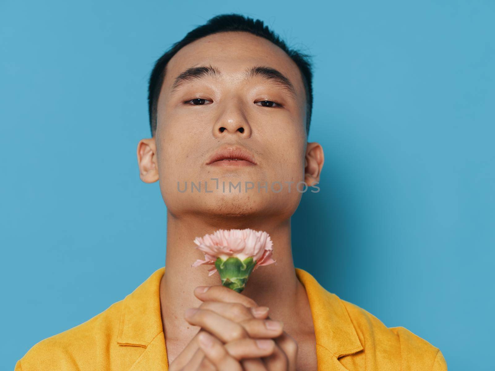 Cute Asian man with a flower near his face on a blue background tilted his head back. High quality photo