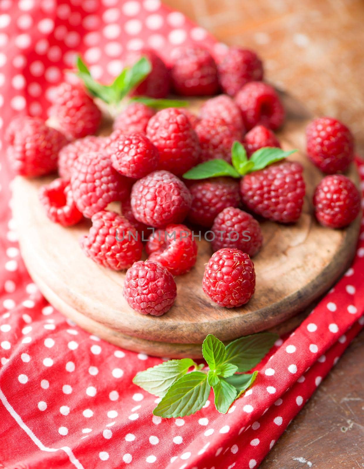 Ripe sweet raspberries in bowl on wooden table.