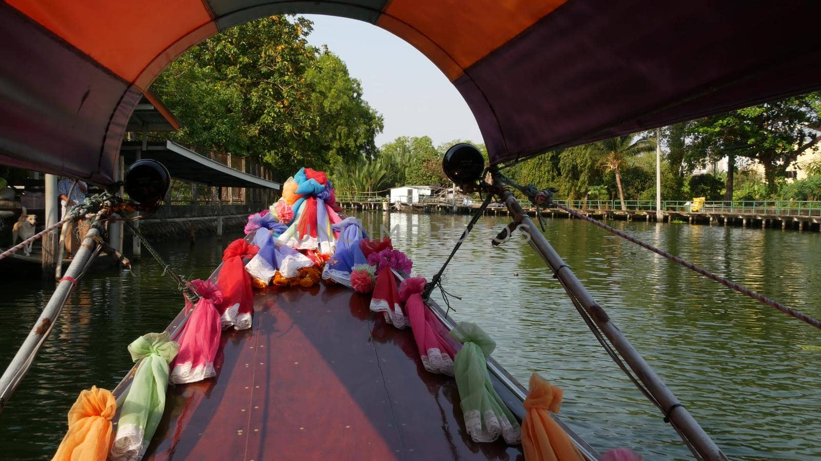 Tourist trip on Asian canal. View of calm channel and residential houses from decorated traditional Thai boat during tourist trip in Bangkok