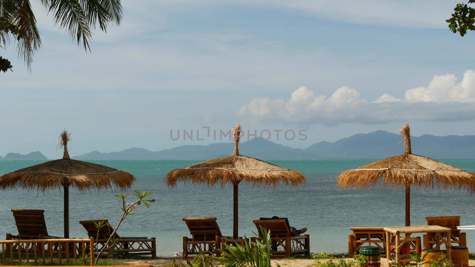 Sunshades on sea background. Sun umbrellas from straw and palm trees on ocean and sky background in Thailand. Relax, Travel vacation holiday resort concept