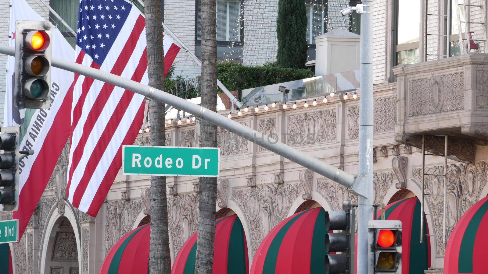 World famous Rodeo Drive Street Road Sign in Beverly Hills against American Unated States flag. Los Angeles, California, USA. Rich wealthy life consumerism, Luxury brands, high-class stores concept