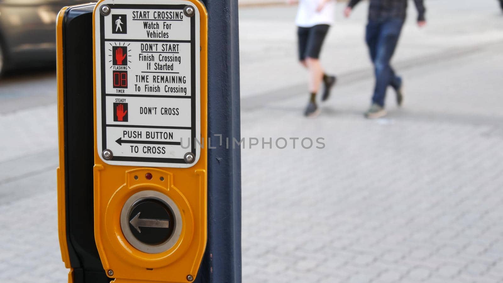 Traffic light button on pedestrian crosswalk, people have to push and wait. Traffic rules and regulations for public safety in USA. Zebra street crossing on road intesection in San Diego, California.