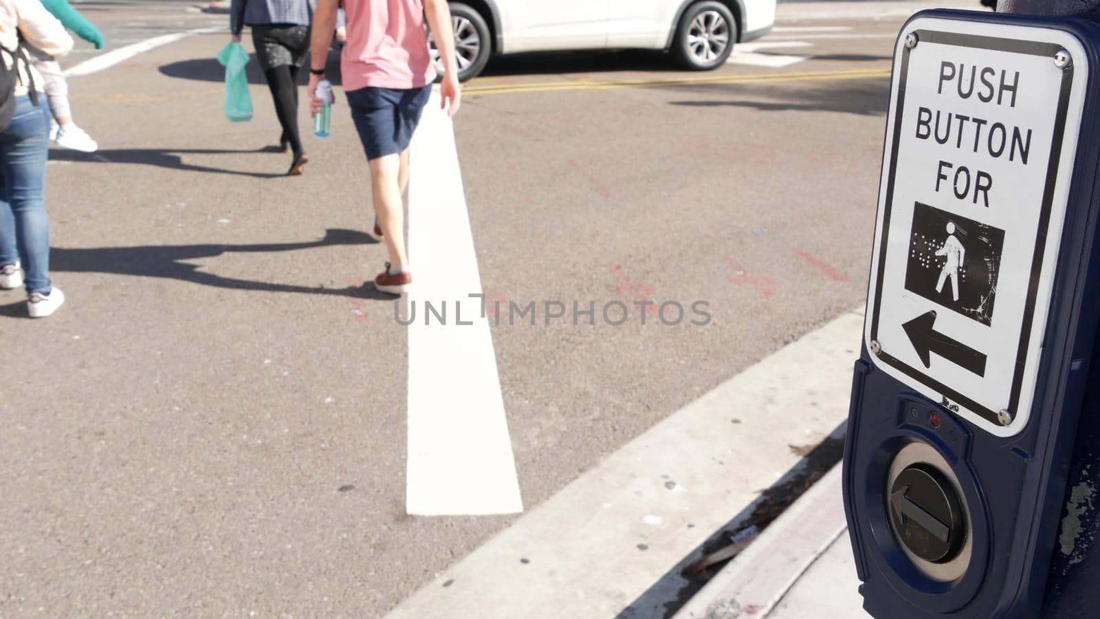 Traffic light button on pedestrian crosswalk, people have to push and wait. Traffic rules and regulations for public safety in USA. Zebra street crossing on road intesection in San Diego, California.