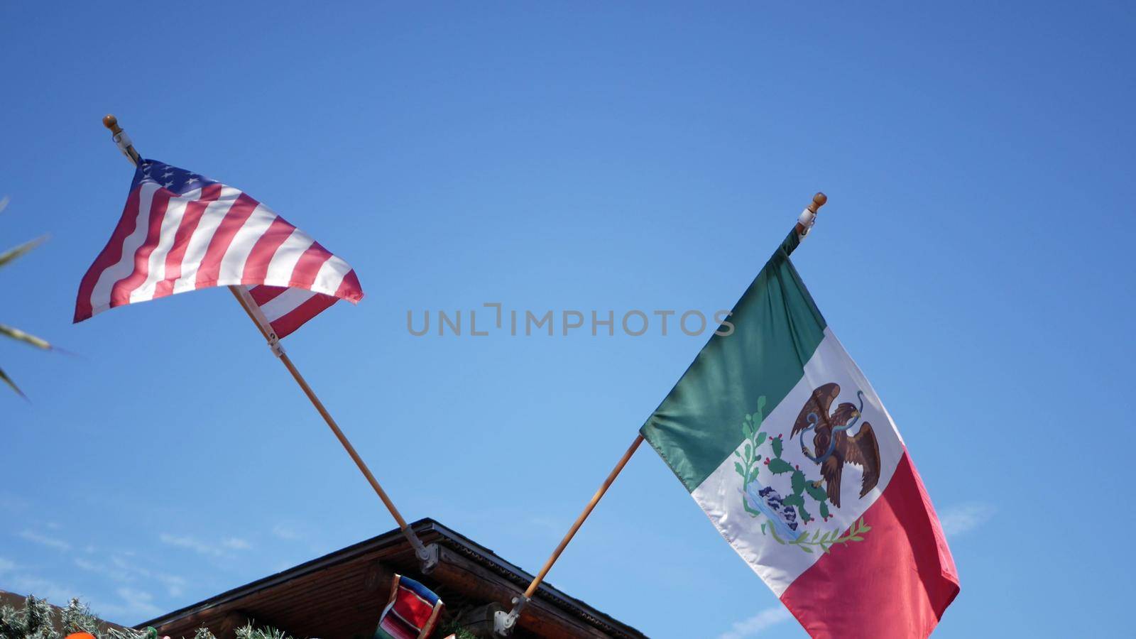 Mexican tricolor and American flag waving on wind. Two national icons of Mexico and United States against sky, San Diego, California, USA. Political symbol of border, relationship and togetherness by DogoraSun