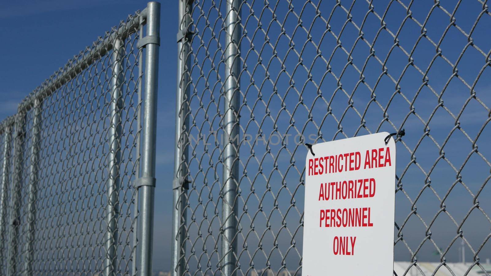 Restricted area, authorized personnel only sign in USA. Red letters, keep off warning on metal fence, United States border symbol. No trespassing notice means violators will be prosecuted by US law.