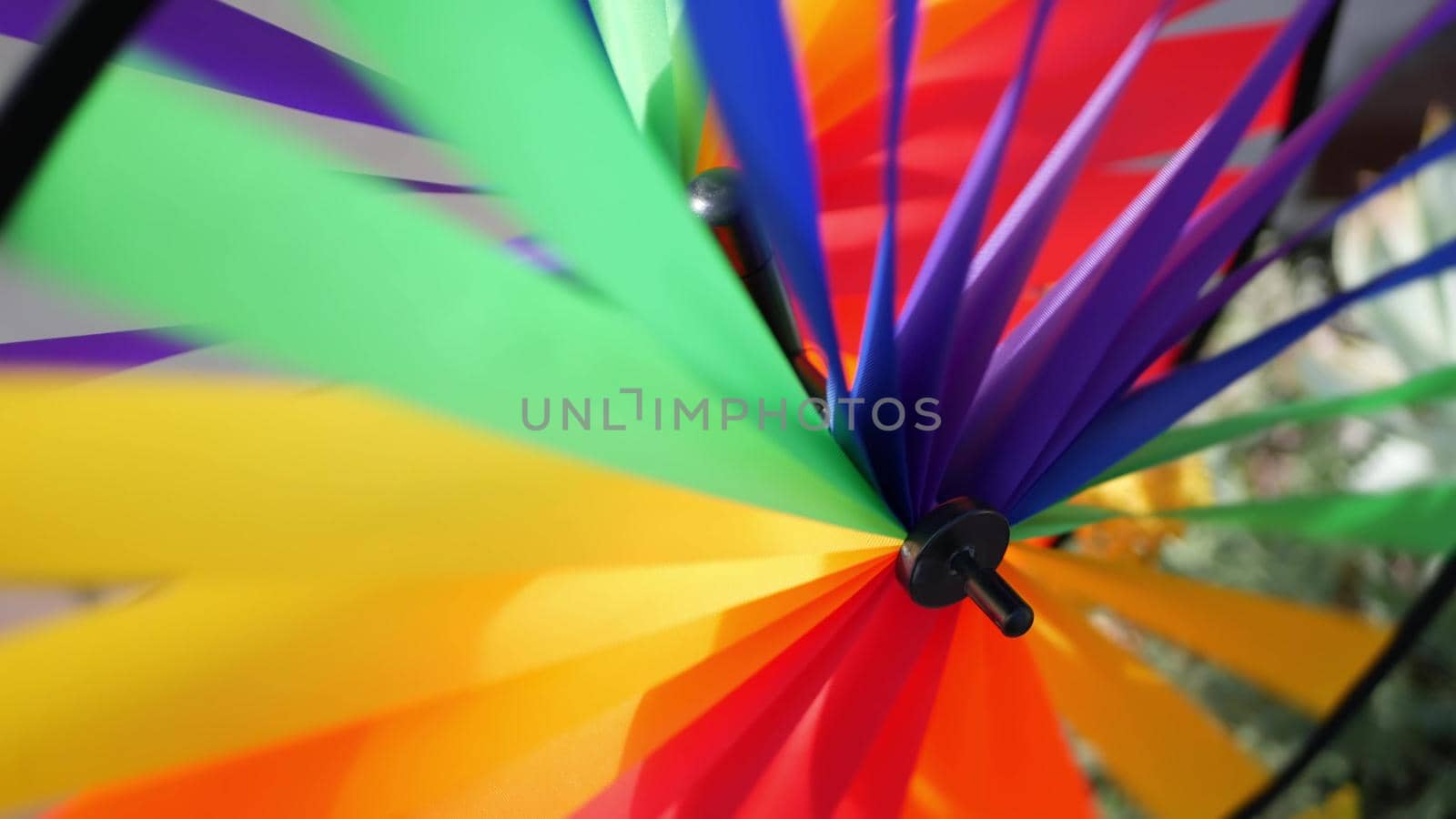 Colorful pinwheel spinning, weather wind vane, garden decoration in USA. Rainbow symbol of childhood, fantasy and imagination rotating. Multi colored spiral toy turning in breeze. Summertime dreaming.