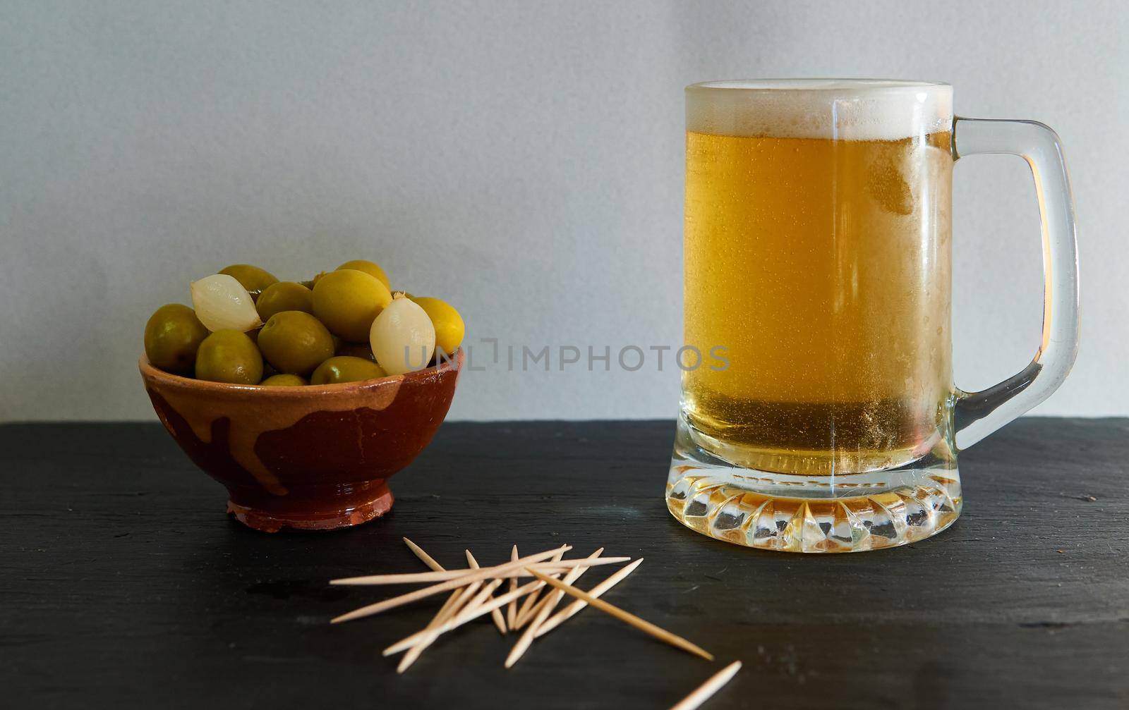 Beer with olives and potatoes with chopsticks on a black base
