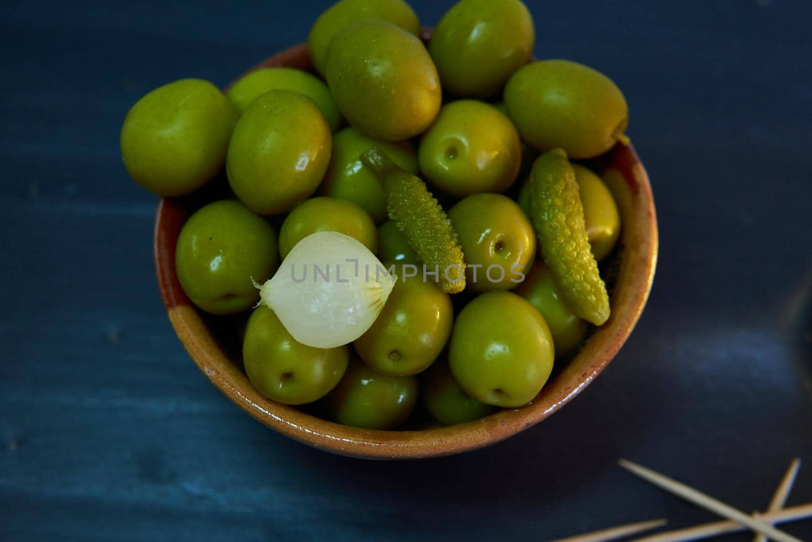 Bowl with green olives with chopsticks on a black background
