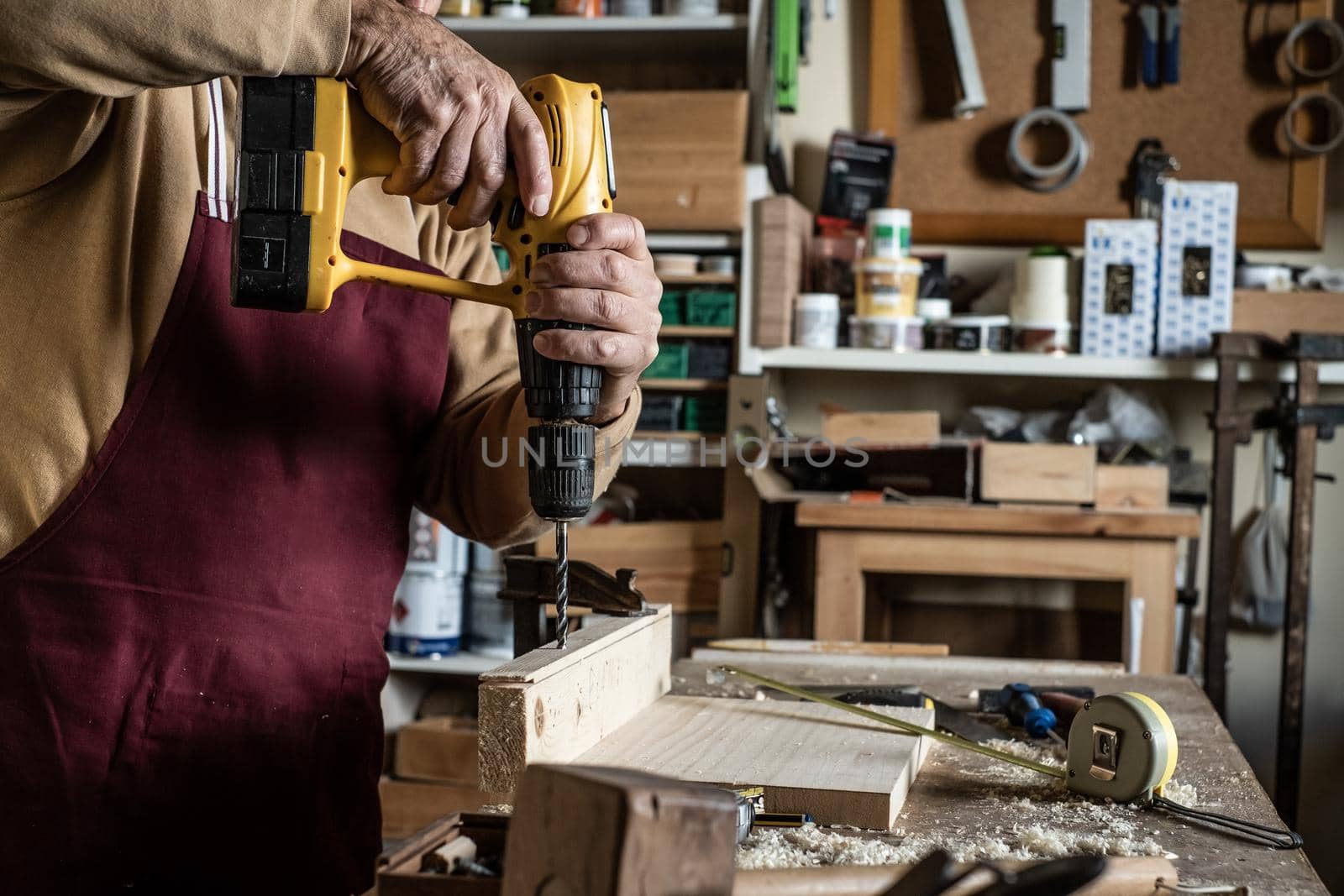 Carpenter with a yellow drill making a hole with a wooden drill on board