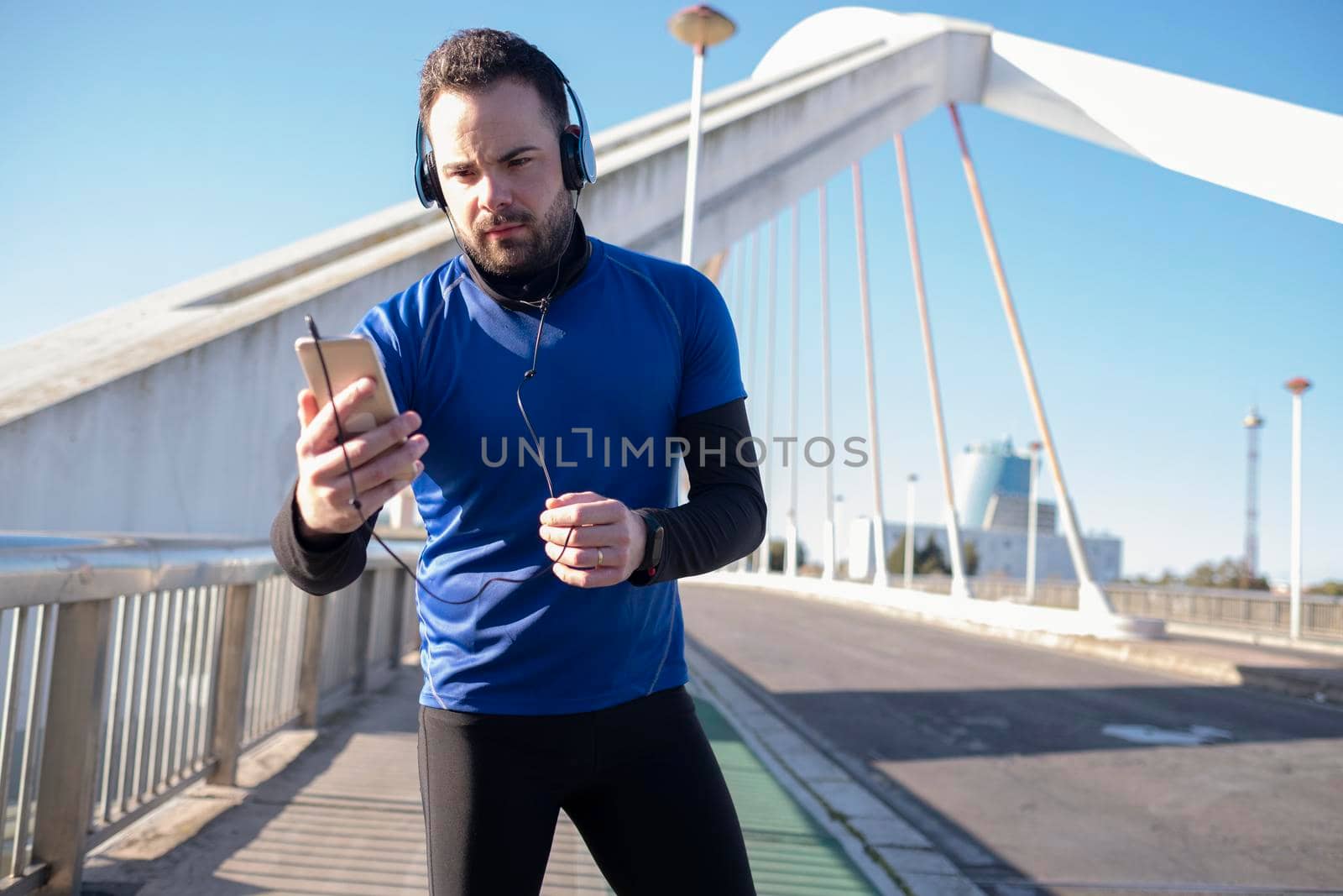 Closeup shot of a male in blue headphones using his mobile while jogging in the street