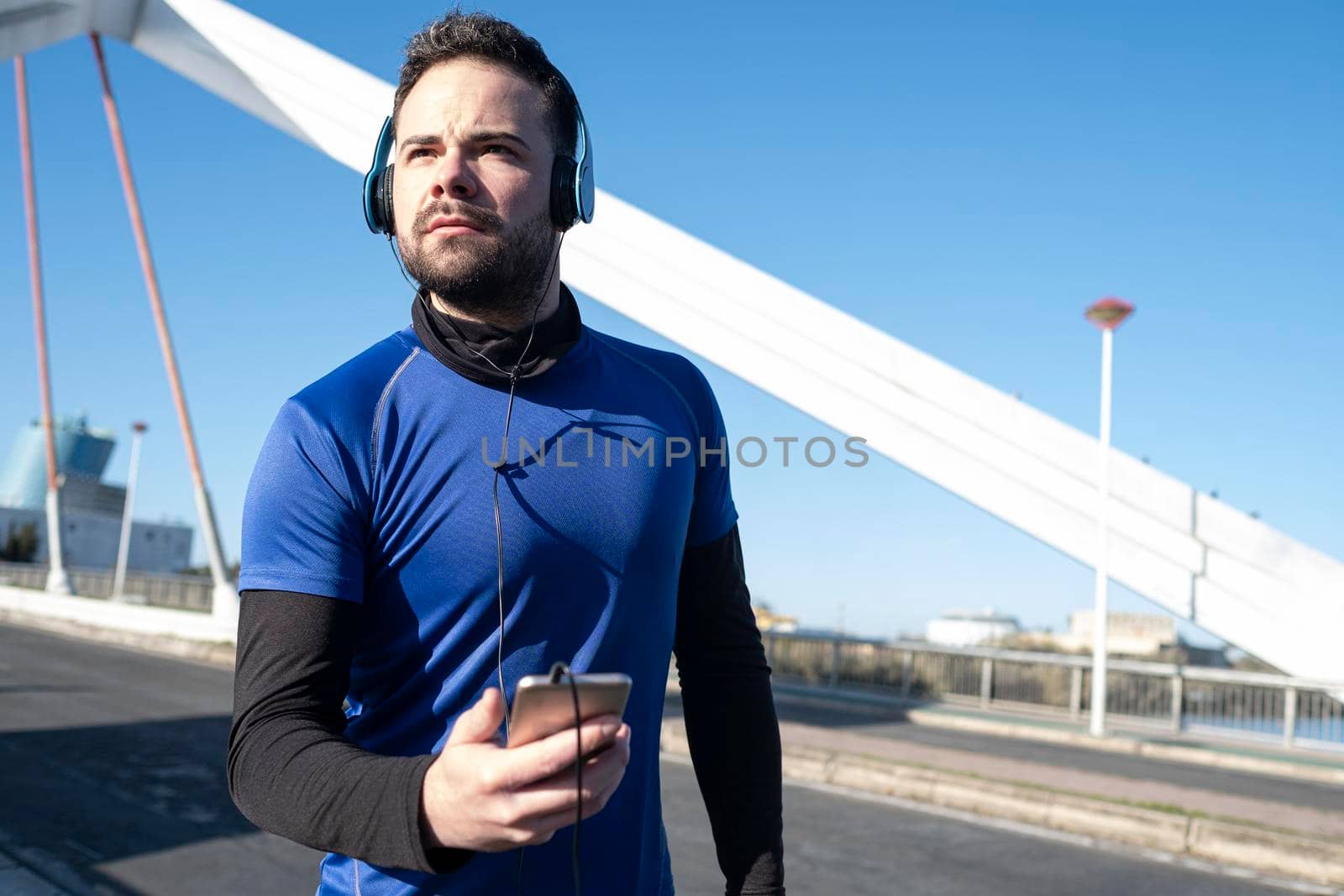 young man looking at his cell phone to listen to music while running through an urban area