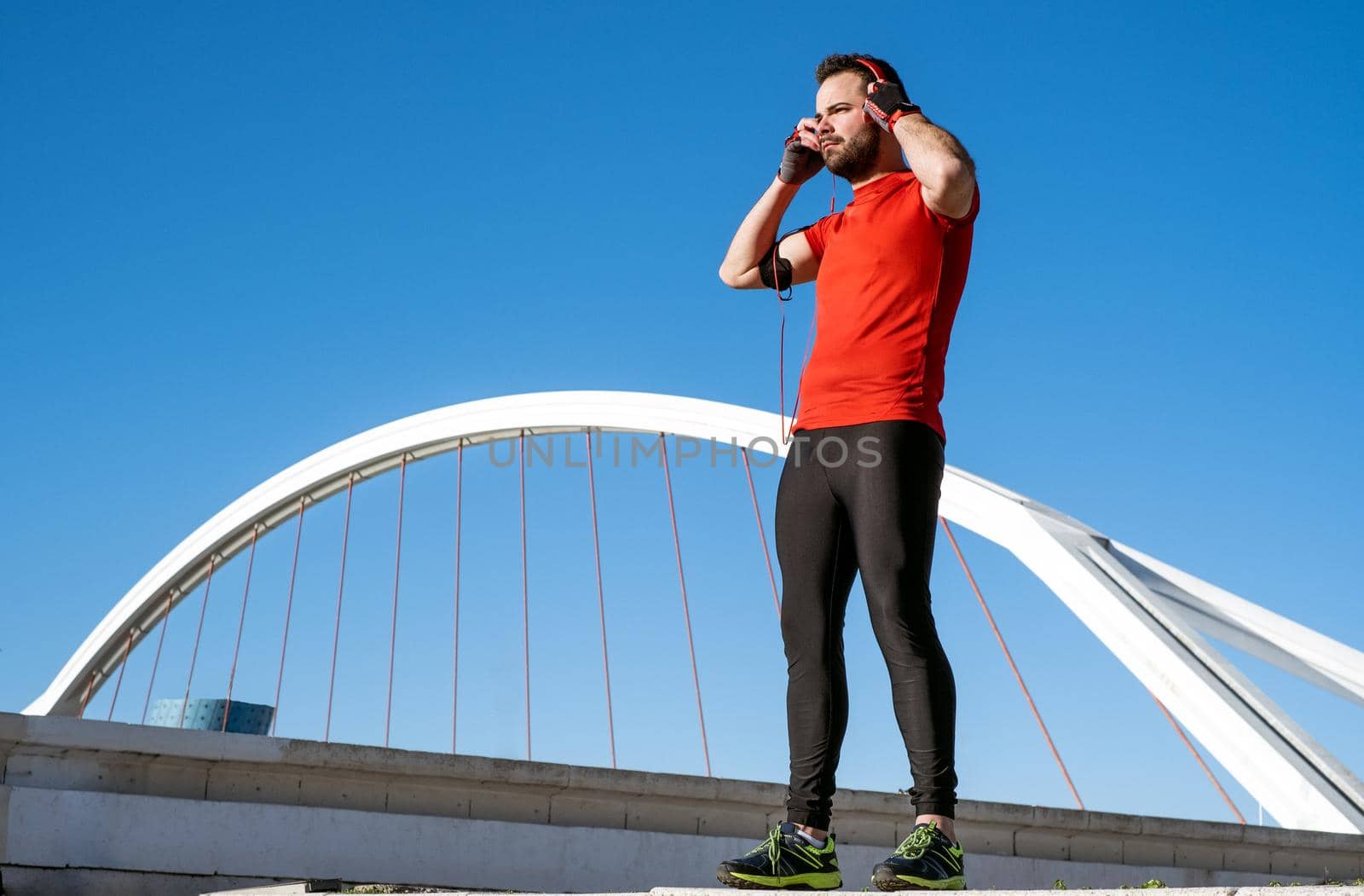 young man preparing to run with a pair of headphones in front of a bridge by soymicrostocker