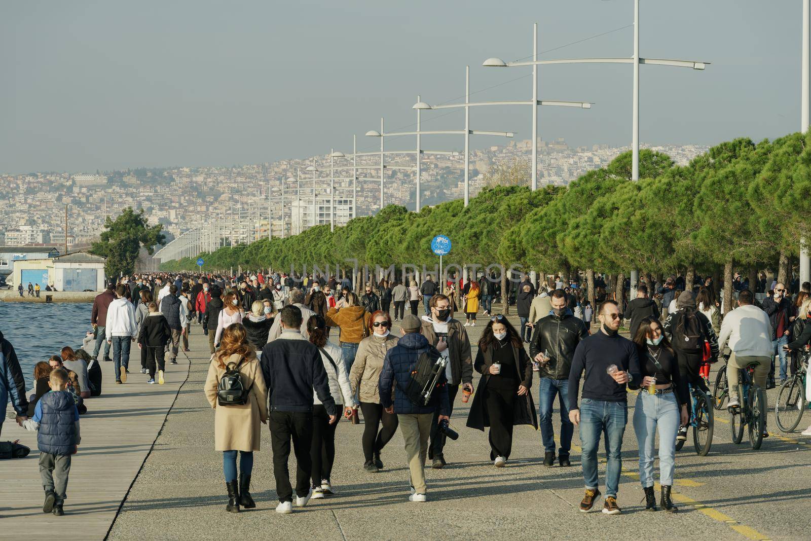 Unidentified persons with face protection walk at close distance on the pedestrian area of the city waterfront in Thessaloniki, Greece.