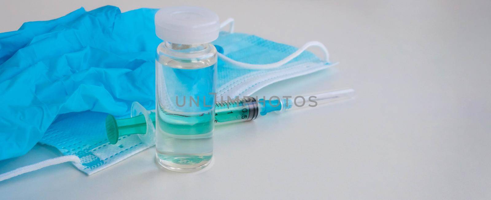 A syringe, gloves, mask, and a bottle of vaccine stand on a blue background. For the prevention, immunization and treatment of coronavirus infection. The concept of medicine and health care.