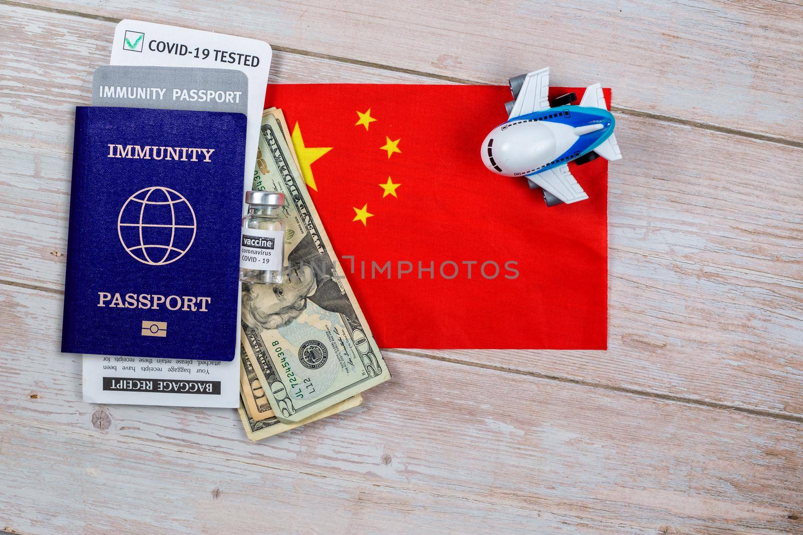 Concept of immunity to coronavirus. Certificate stating that person is not contagious. Passport with note covid-19 test passed, money, vaccine bottle and a toy plane on flag of China
