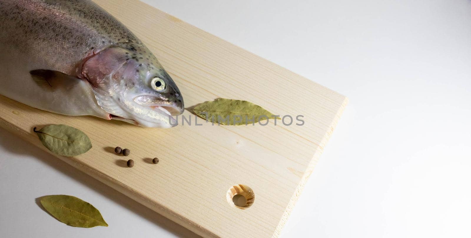 Half a trout fish with its mouth open lies on a wooden board on a white background.