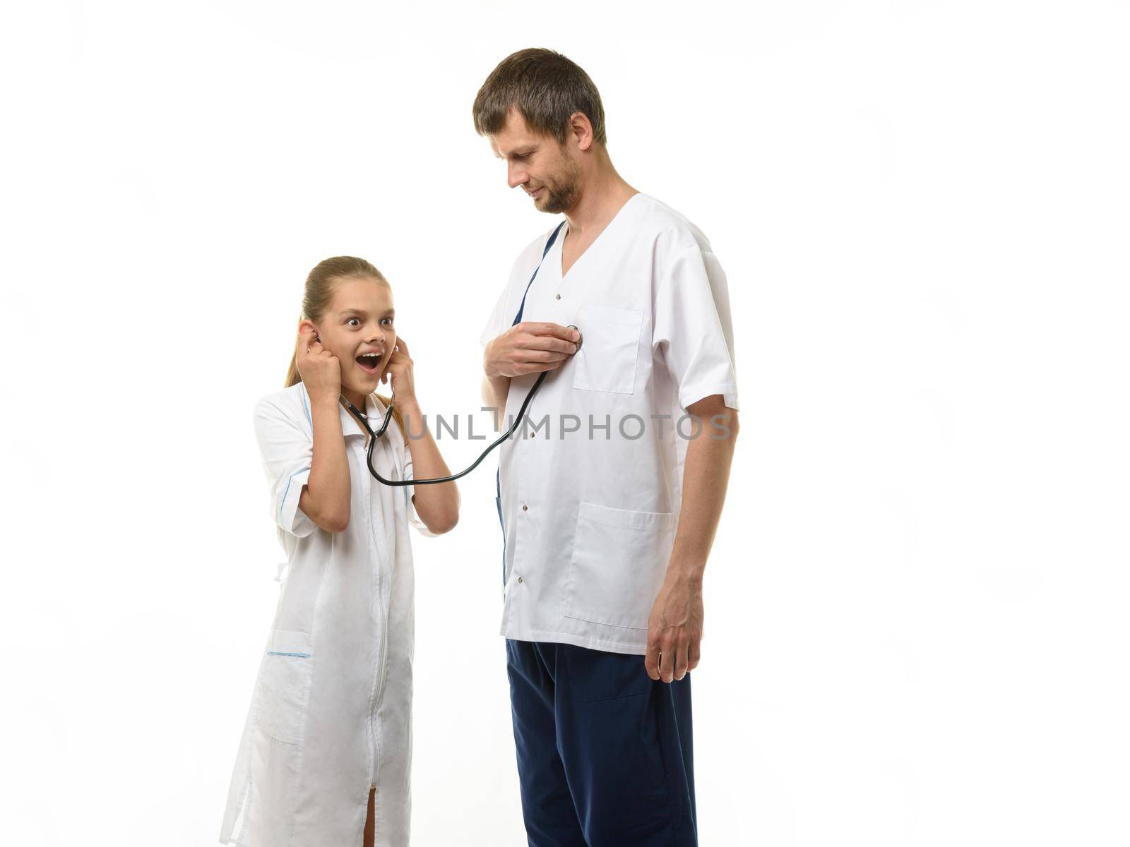The doctor put the head of the phonendoscope to his heart, a girl in a medical coat listens with surprise to the doctor's heart