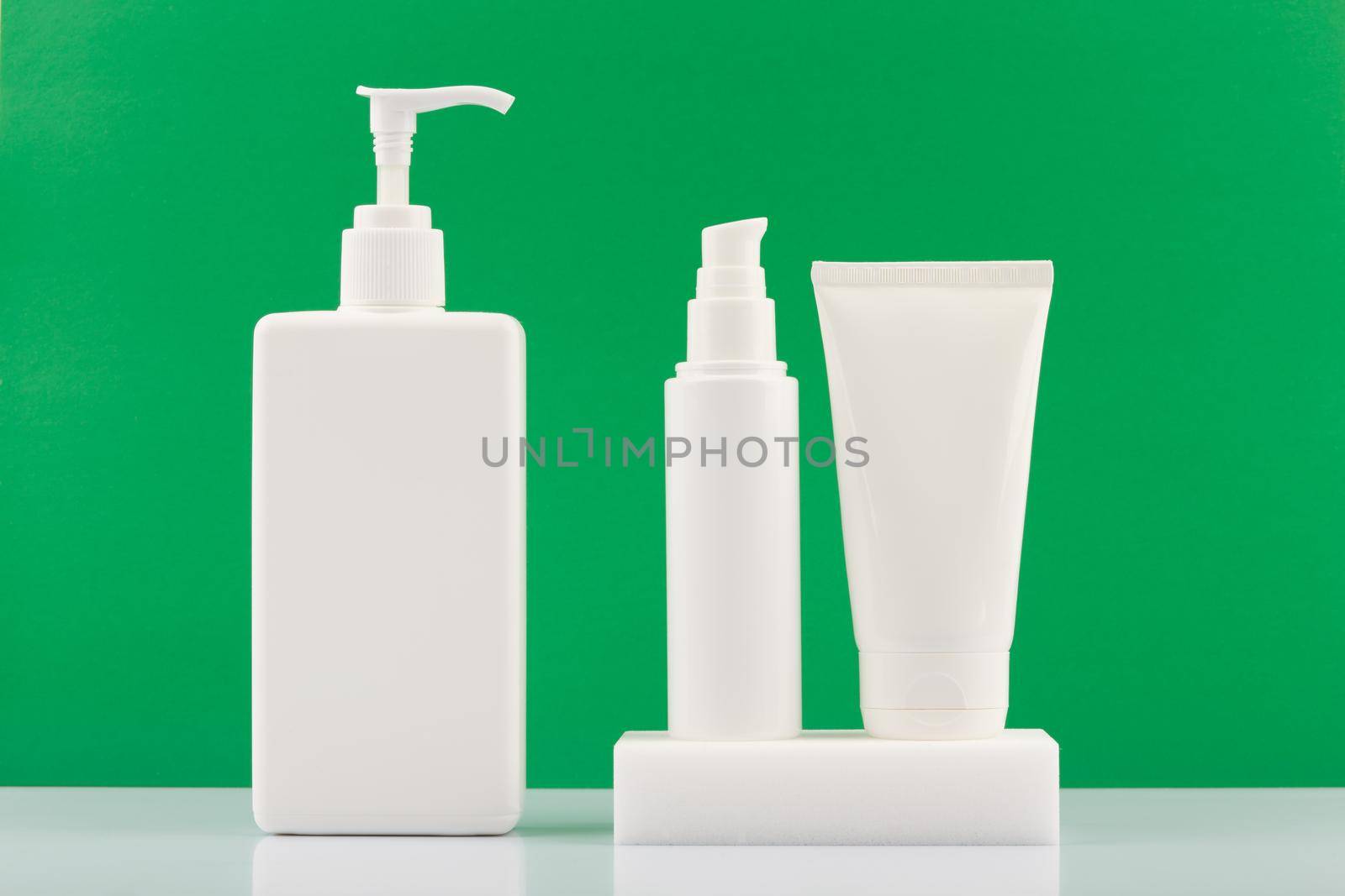 Skincare products in white plastic tubes on white table against green background. Concept of organic beauty products for fresh, young looking skin. Moisturizing or anti aging products.