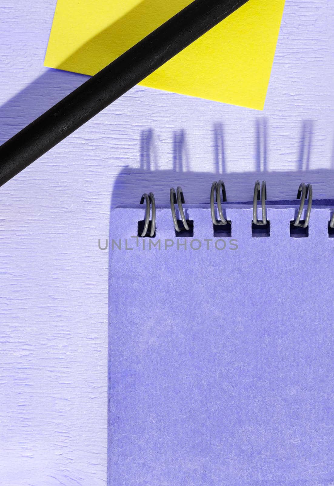 Yellow stick note with black pencil and closed notebook on wooden table