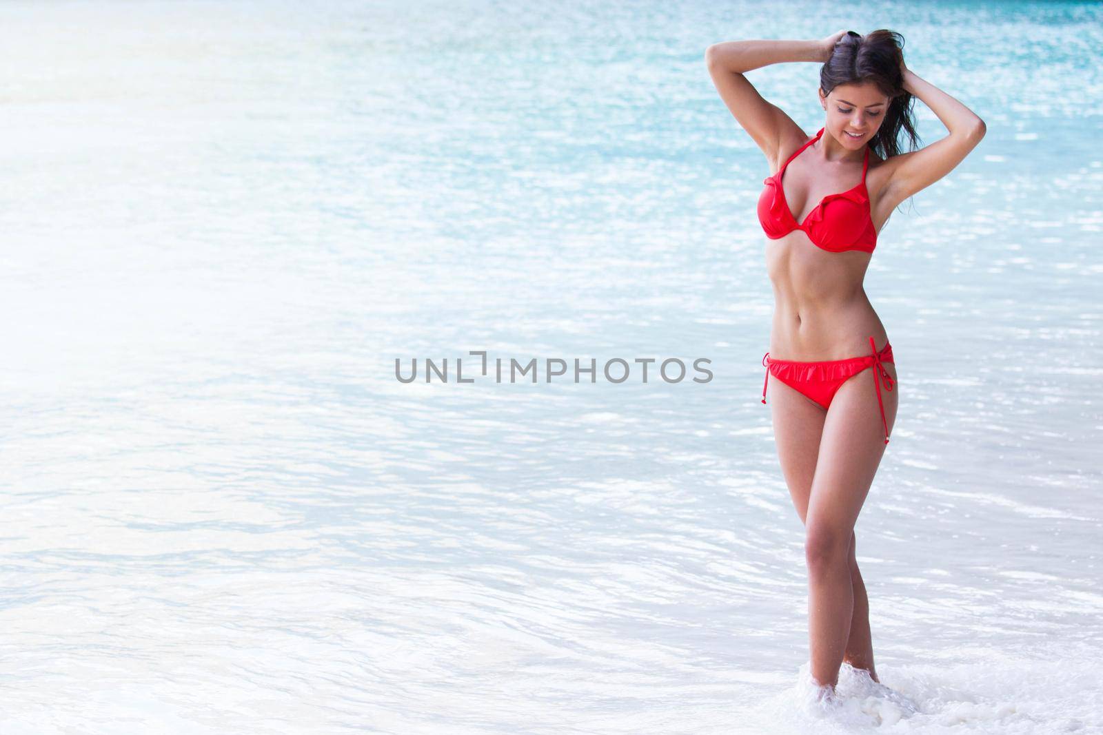 Beautiful smiling woman on summer vacation posing in front of the ocean in her red bikini