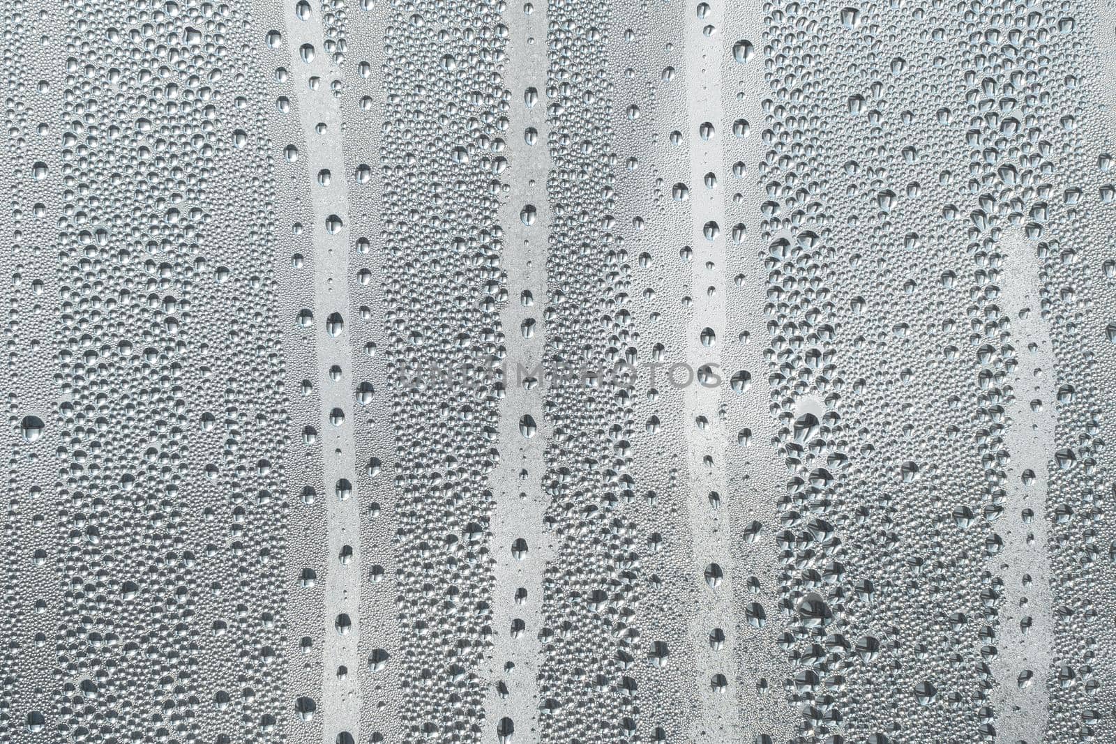 Abstract background ornament with water drops.Raindrops on the glass in rainy weather.The glittering, shiny surface of water on glass.Water drops in the form of balls or spheres.Grey raindrops