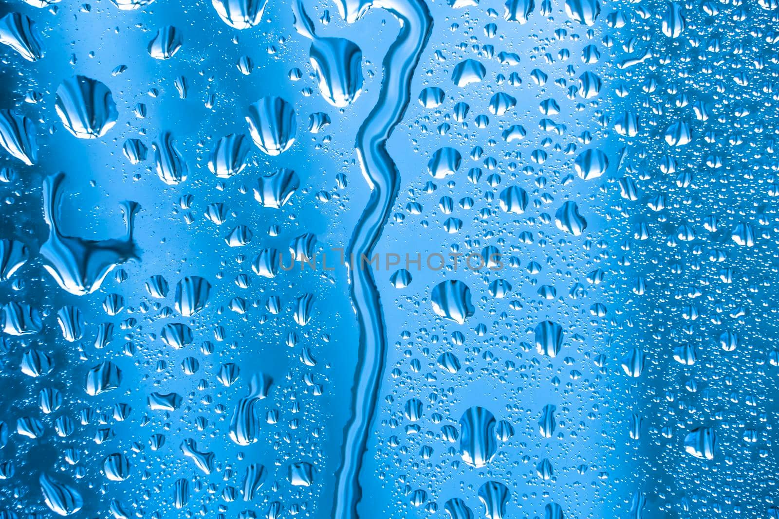 Abstract background ornament with water drops.Raindrops on the glass in rainy weather.The glittering, shiny surface of water on glass.Water drops in the form of balls or spheres.Blue raindrops