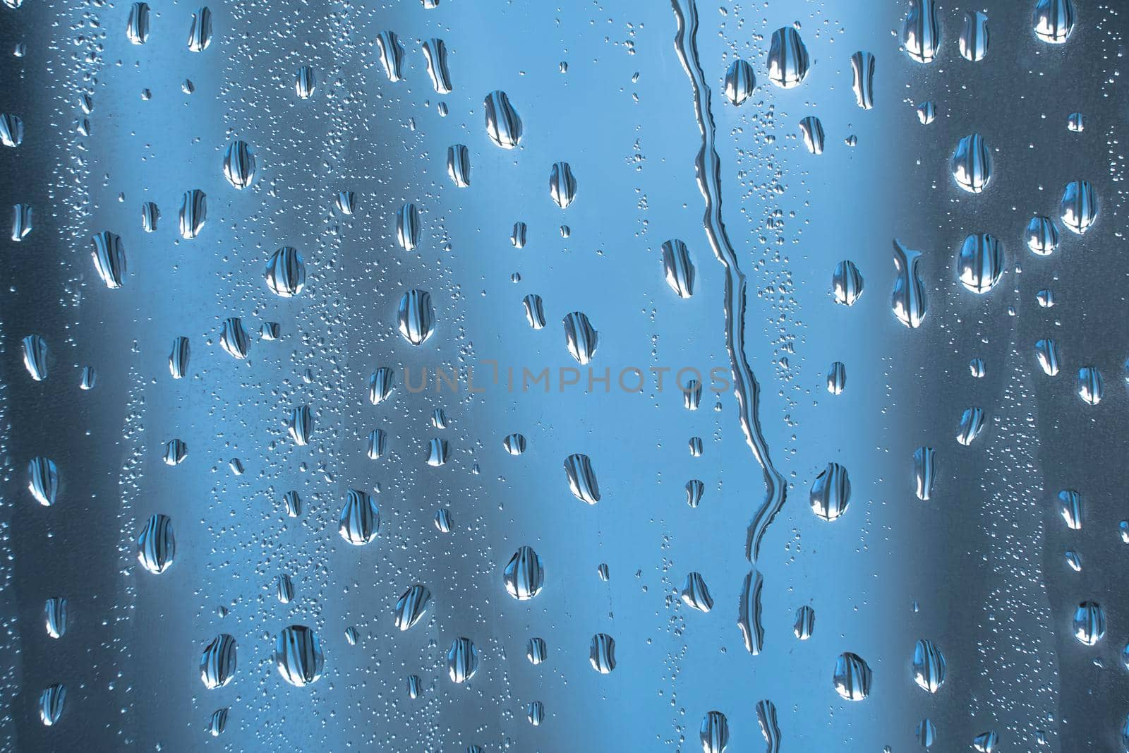 Abstract background ornament with water drops.Raindrops on the glass in rainy weather.The glittering, shiny surface of water on glass.Water drops in the form of balls or spheres.Blue raindrops