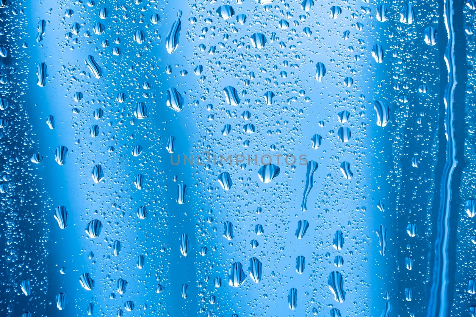 Raindrops on the glass in rainy weather.The glittering, shiny surface of water on glass.Water drops in the form of balls or spheres.Blue raindrops background. Abstract backgrounds ornament with water by YevgeniySam