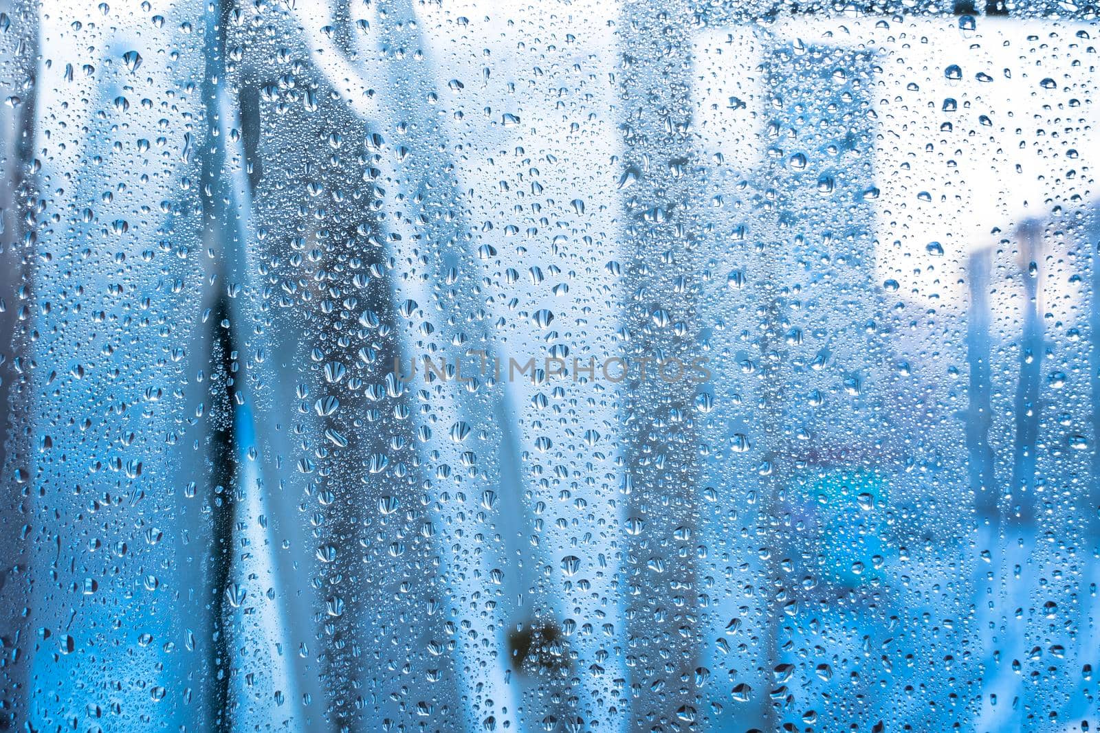 Raindrops on the glass in rainy weather.The glittering, shiny surface of water on glass.Water drops in the form of balls or spheres.Blue raindrops background. Abstract backgrounds ornament with water