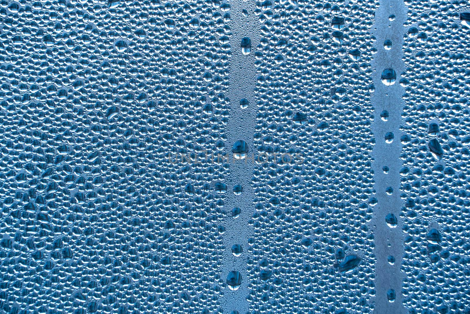 Abstract background ornament with water drops.Raindrops on the glass in rainy weather.The glittering, shiny surface of water on glass.Water drops in the form of balls or spheres.Blue raindrops