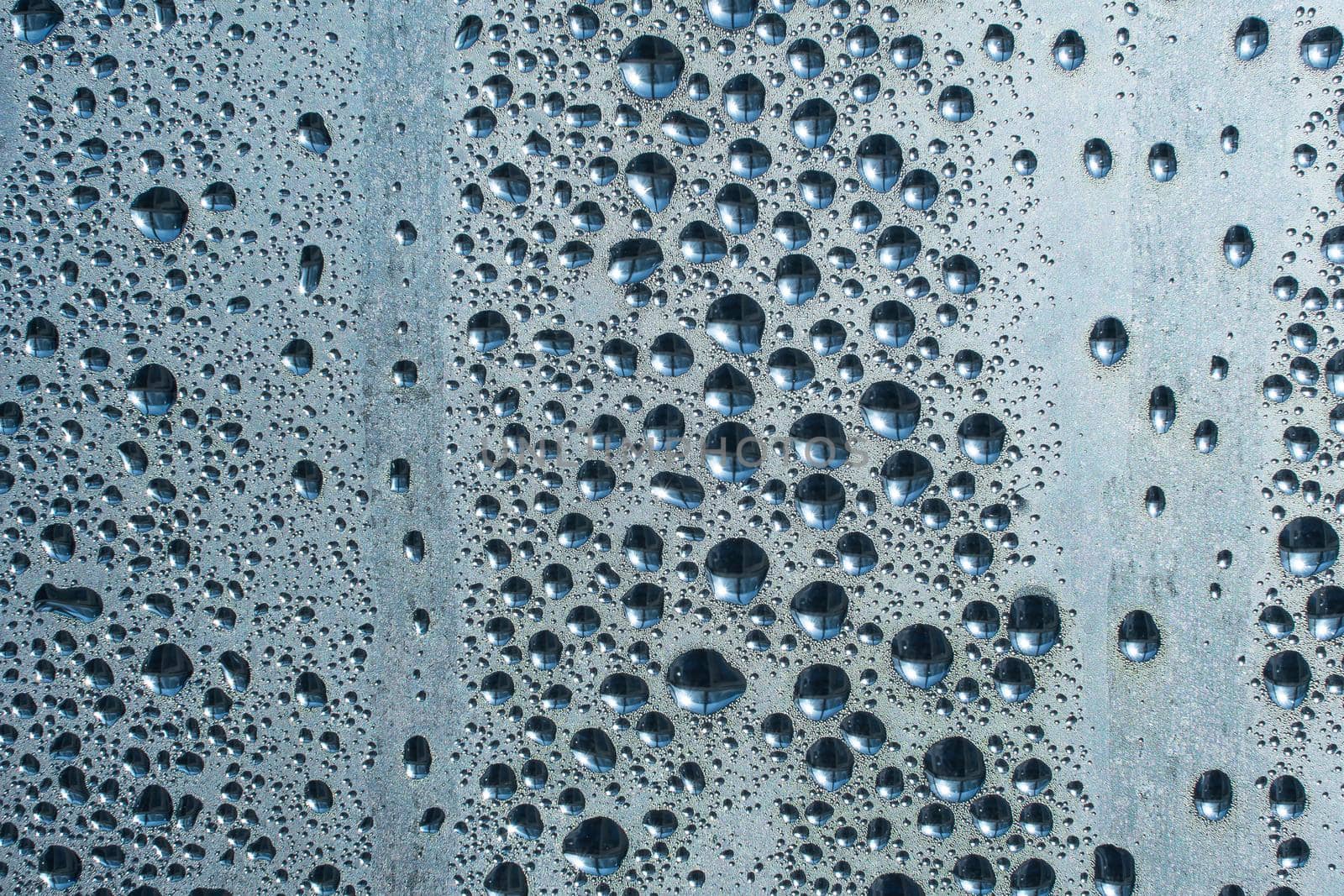 Raindrops on the glass in rainy weather.The glittering, shiny surface of water on glass.Water drops in the form of balls or spheres.Blue raindrops background. Abstract backgrounds ornament with water by YevgeniySam