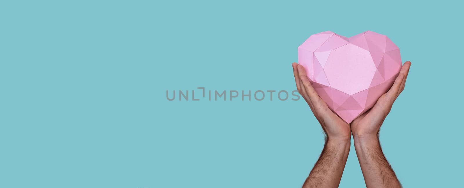 A large pink paper heart in a man's hands. Polygonal heart on a blue background. Banner. Hands close-up. concept for valentine's day, wedding day, love. Mock up