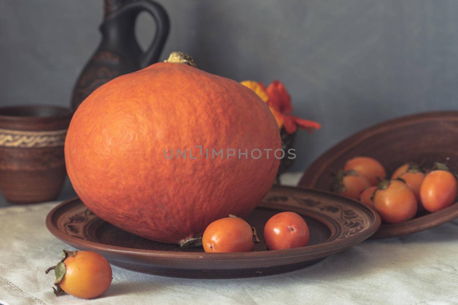Autumn still life with pumpkin and nasturtium flowers. On the table there is a ceramic tableware and a tablecloth made of natural materials.