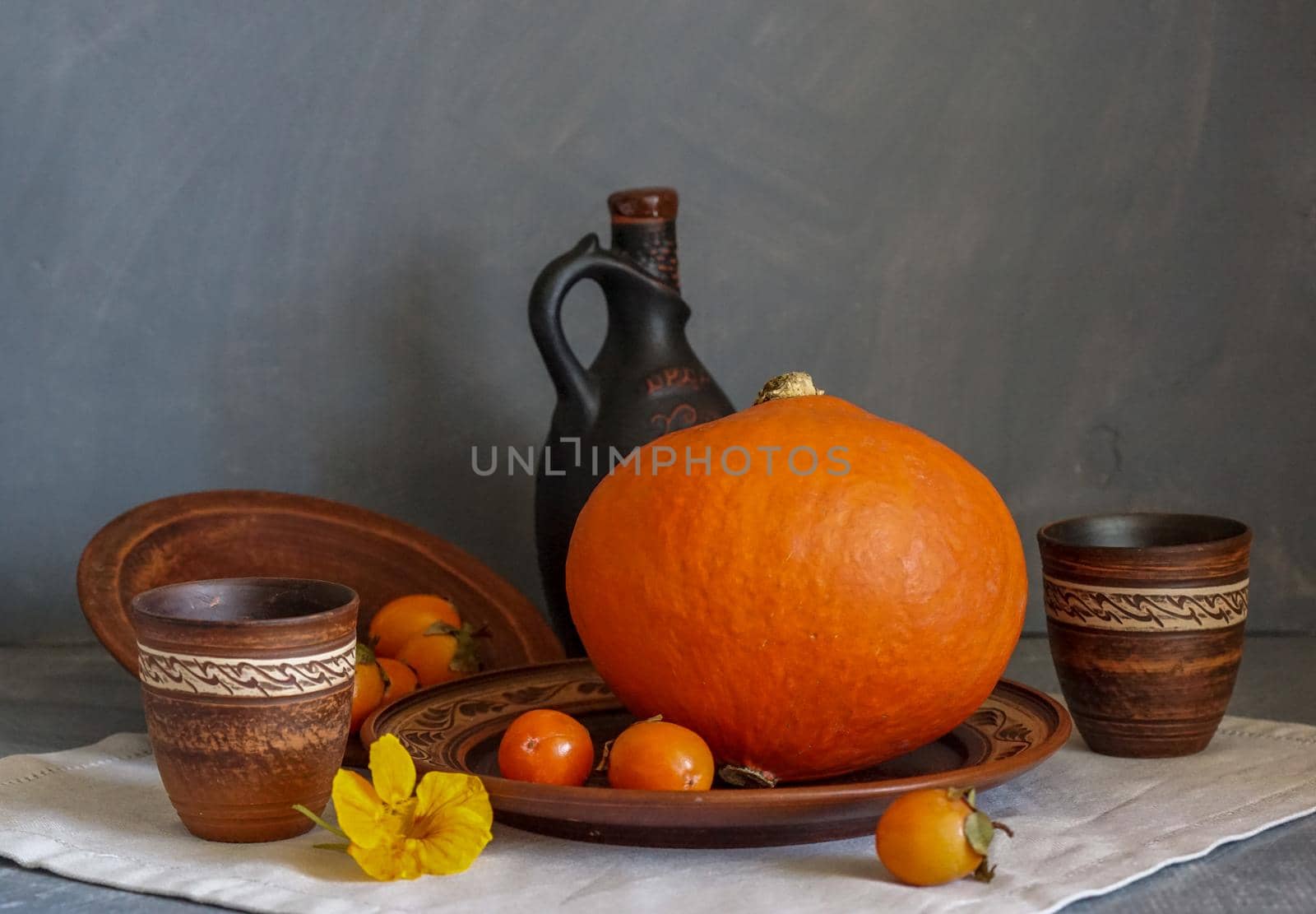 Autumn still life with pumpkin and nasturtium flowers. On the table there is a ceramic tableware and a tablecloth made of natural materials.