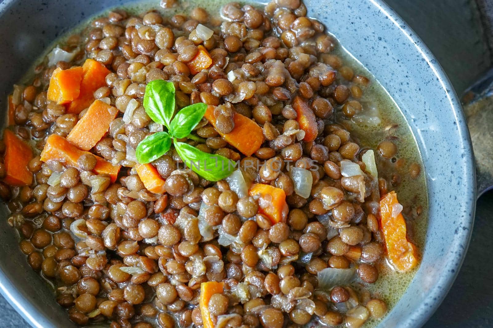 Lentil porridge in a ceramic bowl on the table. Close-up shot. The food is decorated with a sprig of Basil.
