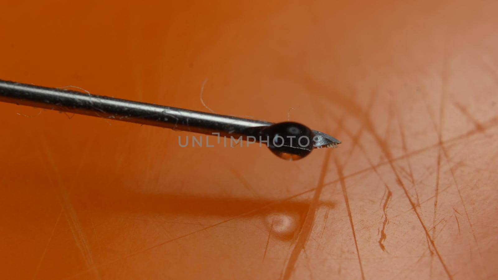 Water drop falling from the syringe needle against orange background by Photochowk