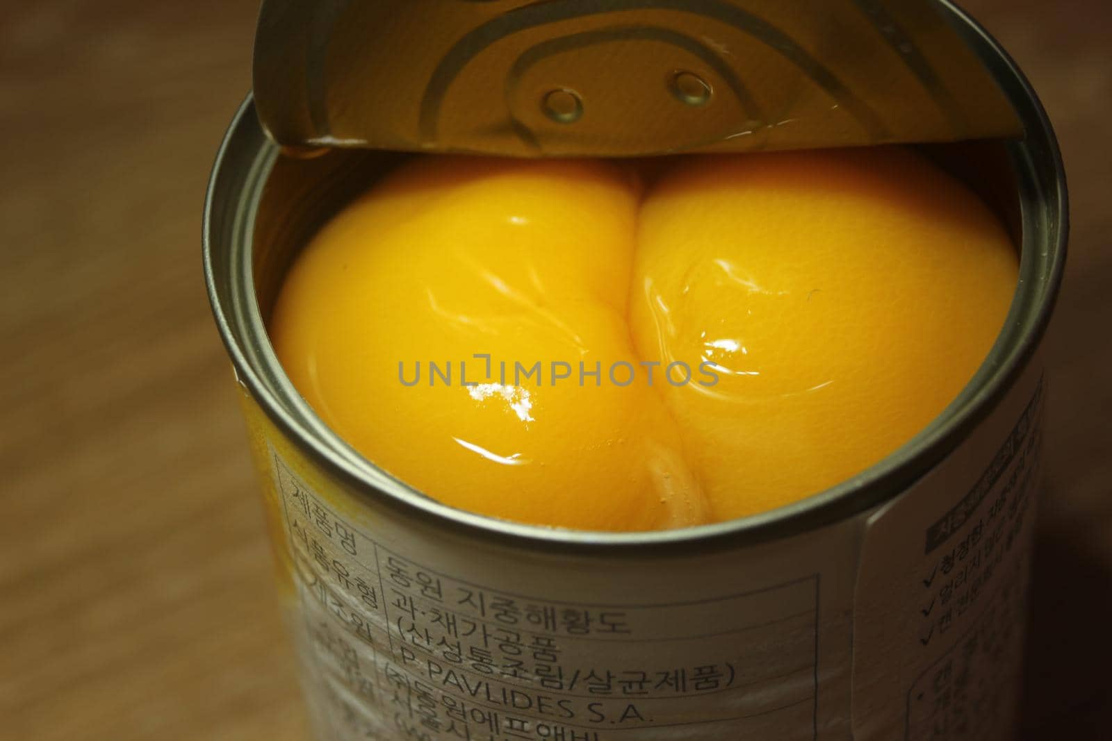 Chuncheon South Korea, October 30-2020: Closeup view with selective focus of yellow peaches slices. Canned peaches halves sprinkled with syrup in a metallic can on wooden floor