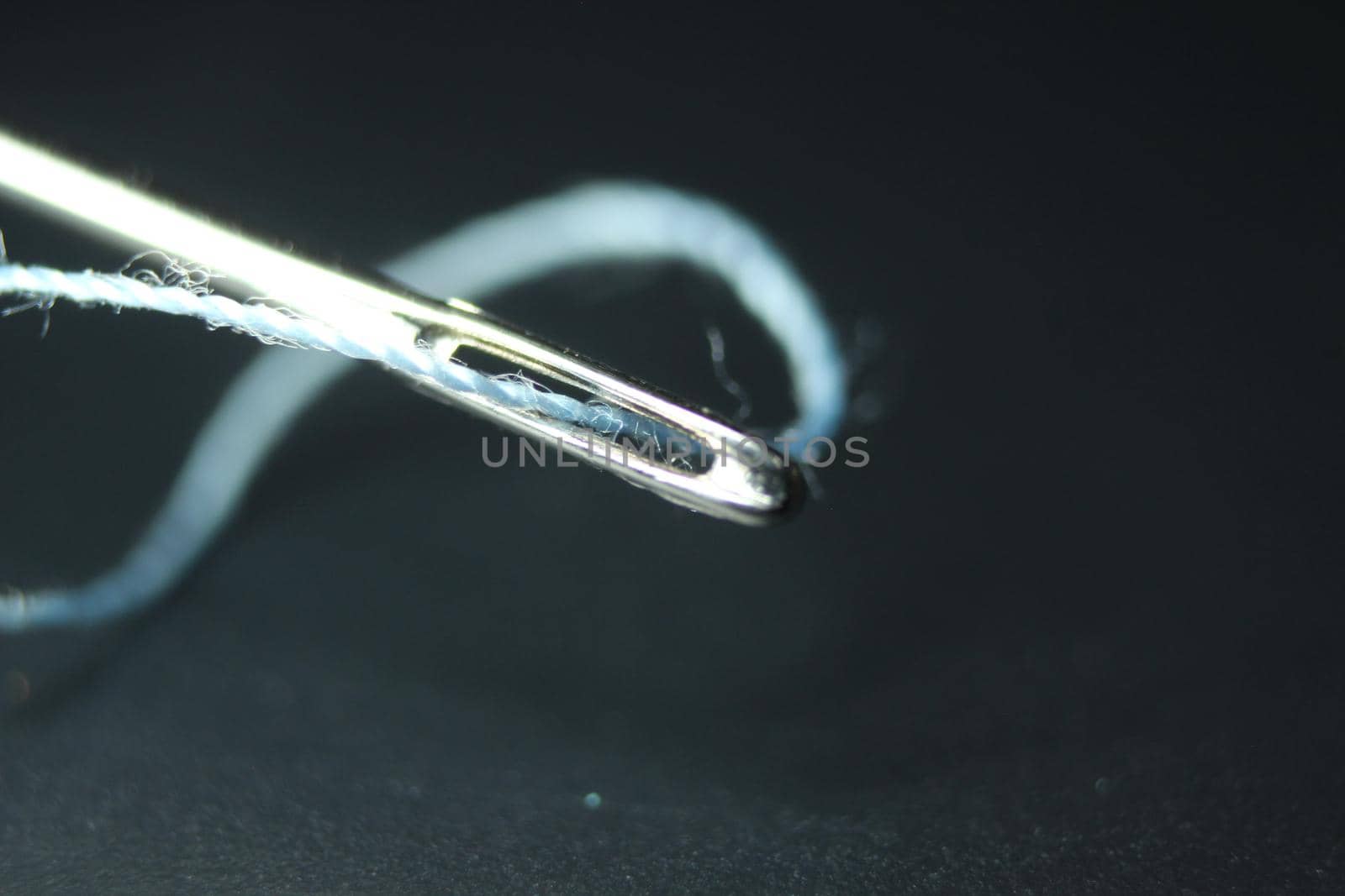 Macro photograph of sewing needle. Small needle with thread in the eyelet, isolated over the black background.