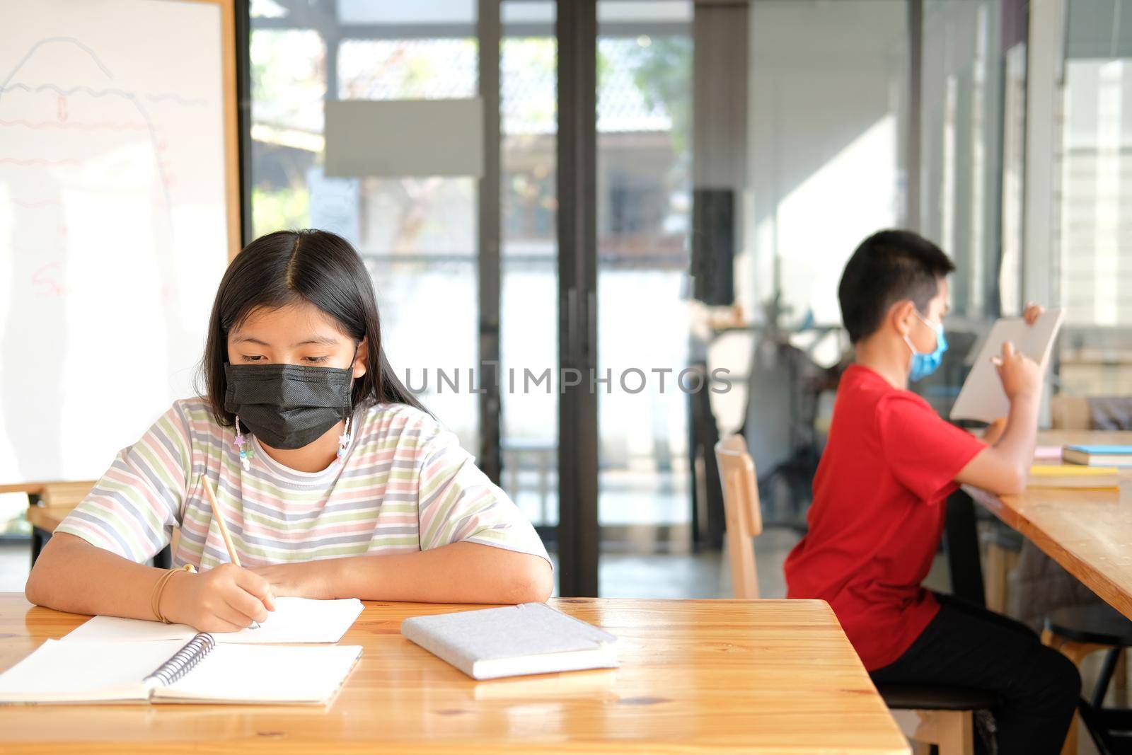 asian girl student wearing face mask studying writing notes doing homework in library. learning education at school