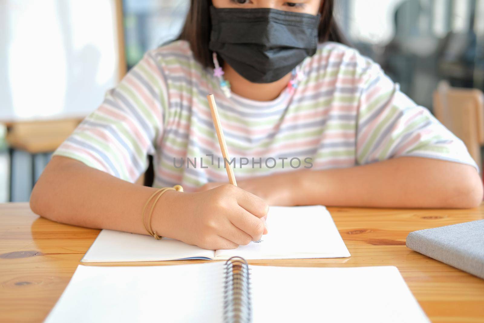 asian girl student wearing face mask studying writing notes doing homework in library. learning education at school