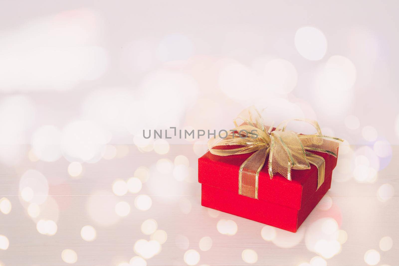 Red gift box on wooden table with bokeh background, love and romance, presents in celebration and anniversary with surprise on desk, happy birthday, copy space, nobody, valentine day concept. by nnudoo